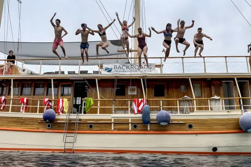 Group of guests jumping off large wood panel boat.