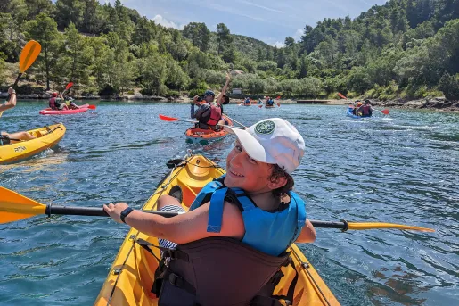 POV shot of guests kayaking, forested coast in distance.