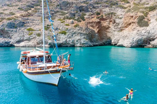 Guests near and on boat, swimming, relaxing, rocky coast nearby.