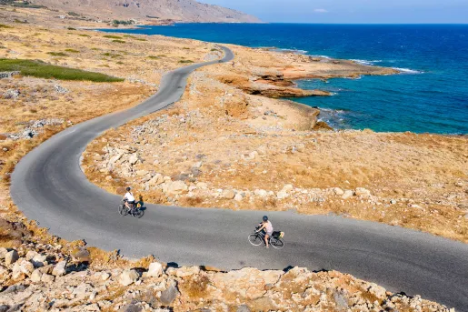 Two guests cycling along golden coastline, ocean to their right.