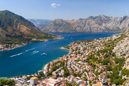 Bird's eye of Croatian riverside city, mountains all around, boats in river.
