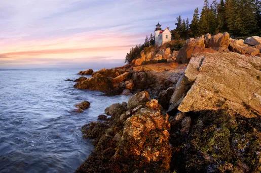 Wide shot of craggy inlet, small white lighthouse, sunset.