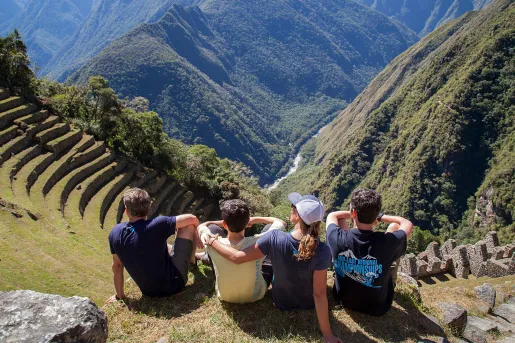 Four guests sitting on Machu Picchu hillside, overlooking mountains. 