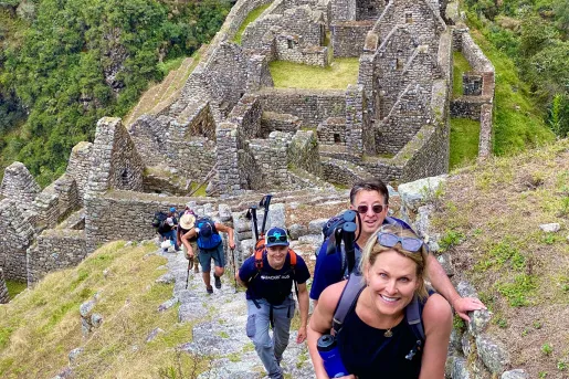 Guests hiking up stone trail, Machu Picchu ruins behind them.
