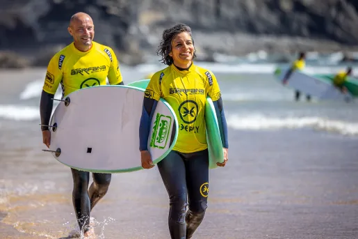 Two people in yellow rash guards carrying surfboards along the beach