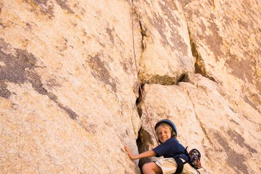 Child rock climbing on sandy cliffside.