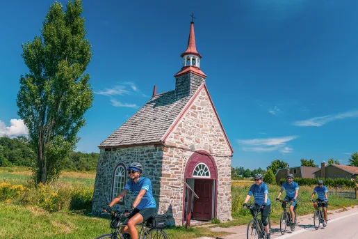 Four guests cycling past small brick building.