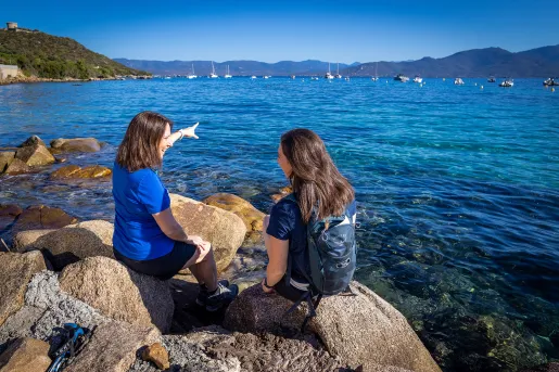 Two guests sitting on large rocks on coast, one pointing towards ocean.