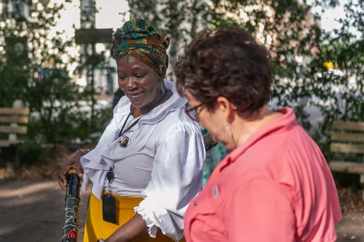Two women talking, one is showing the other a tube-like object.