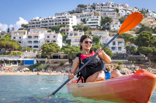 Woman kayaking in turquoise waters with white buildings in the background