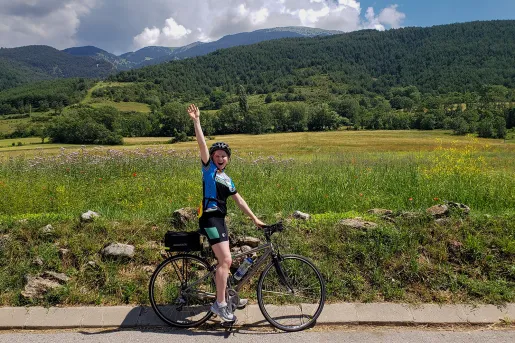 Backroads guest waving at the camera while riding her bike past a green field