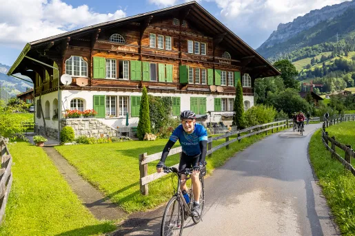Guests cycling past wooden and stone hotel.