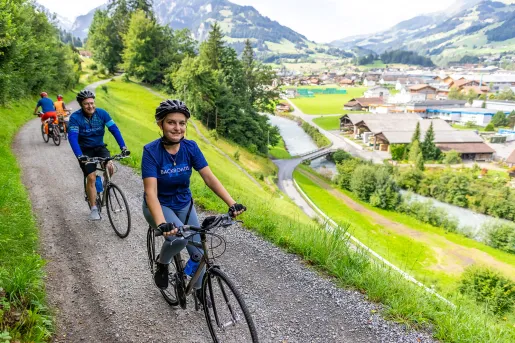 Guests cycling on hillside trail, mountain village below, on their left.