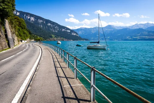 Wide shot of coastal road, blue water, cliffside, small boats.