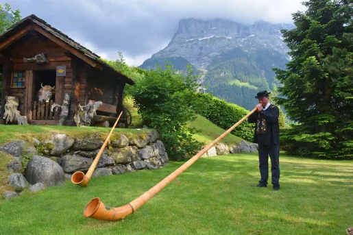 Local man playing a Swiss Horn, wooden shack in background.