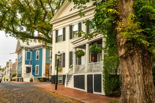 Shot of a residential street, two large, multi-room houses visible.