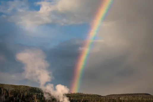 Geyser expelling steam and connecting with the end of a rainbow
