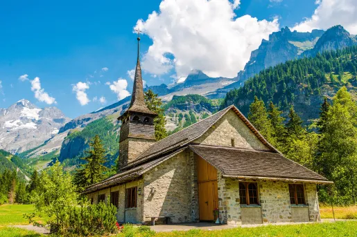 Wide shot of stone cathedral, mountains, clouds in distance.