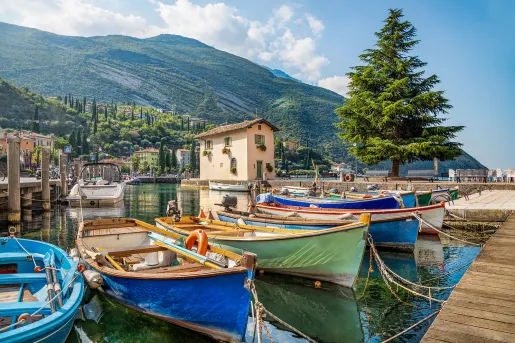 Small coastal pier, colorful ships visible, mountain in distance.