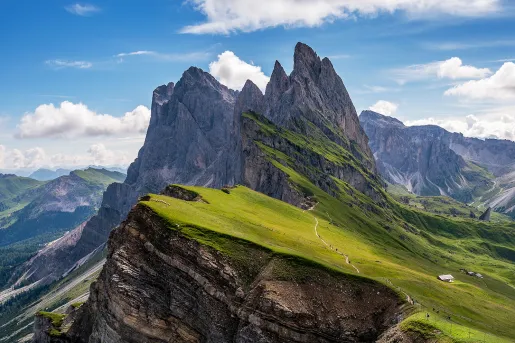Wide shot of craggy, sharp mountain peaks, small house barely visible.