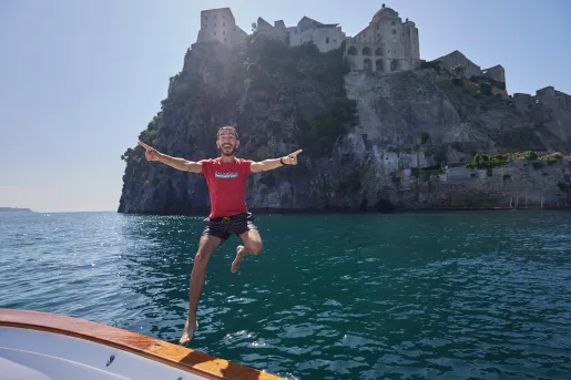 Guest jumping off boat, hilltop house in background.