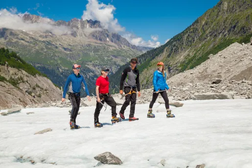 Four guests walking in snow, sweeping mountain range in background.