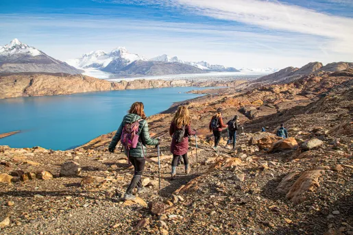 Group of guests walking towards blue lake, snowy mountains in distance. 
