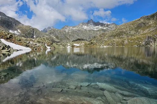 Shot of still lake, craggy rocks dotting lakeside, mountain in distance.
