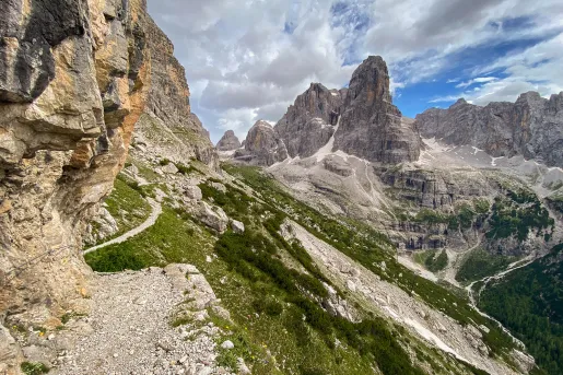 Wide shot of craggy cliffs, trails, valley, mountain in distance.