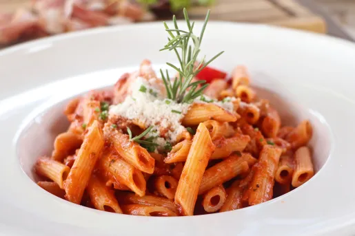 Plate of tomato pasta, cheese, rosemary garnish.