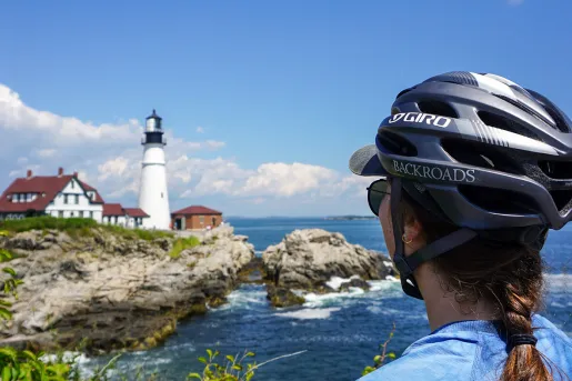 Caucasian woman in a bike helmet looks across a body of water at a lighthouse