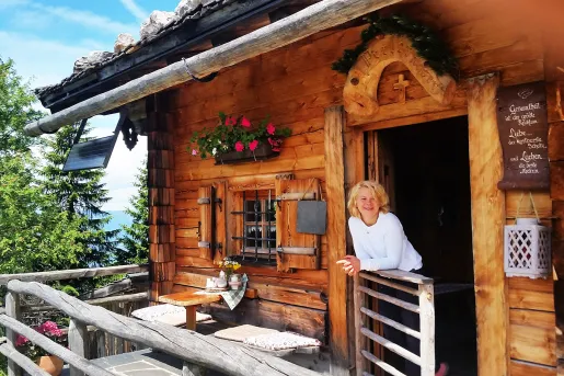 Woman leaning on balcony off of log cabin.