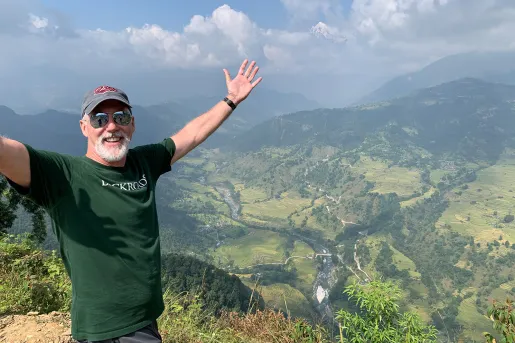Man with arms outstretched above a valley in Nepal