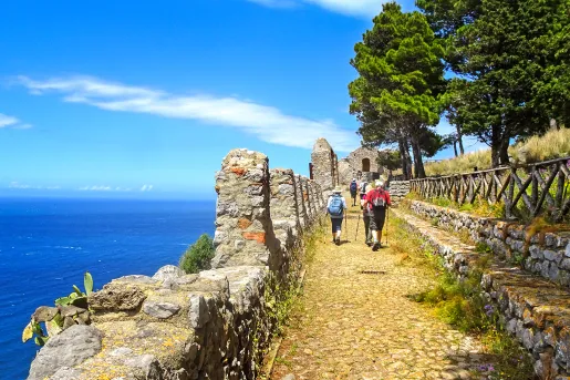 Guests walking next to ocean cliffside, towards small sandstone building.