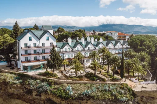 Exterior wide view of white and blue hotel buildings with palm trees in the front