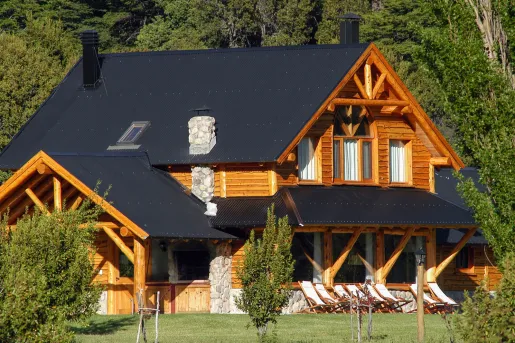 Exterior view of a wooden log cabin with a black roof and a stone chimney