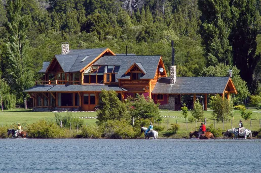 Wide exterior view of a wooden log cabin with a lake in front