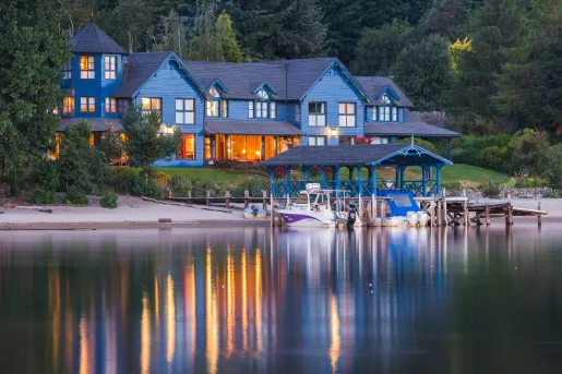 Blue lodge building with a large lake in front with boats docked by a pier
