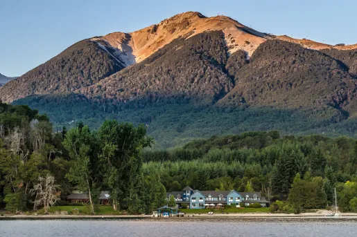 Blue lodge building surrounded by tall trees and a large mountain in the background