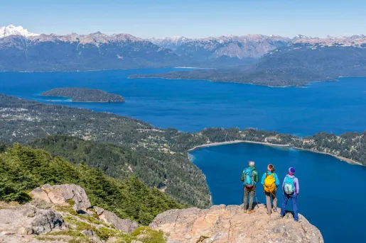 Group of 3 people standing on a cliff, looking out to a lake