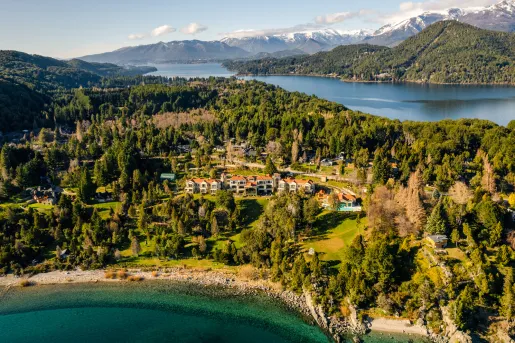 Sky view of white and brown buildings surrounded by a forest and a lake in the distance