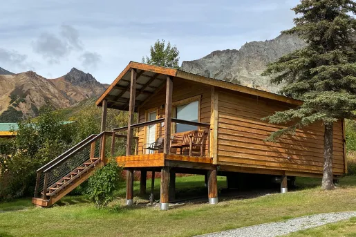 Wooden cabin with a small staircase in front and wooden chairs on the porch