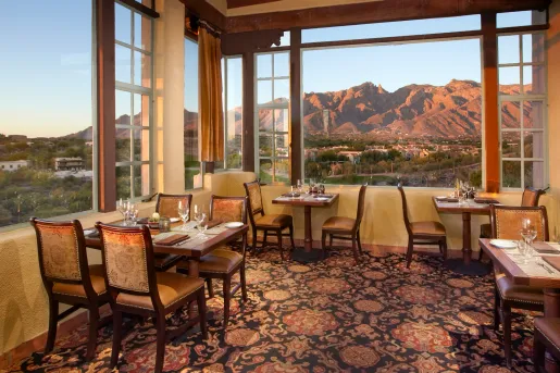 Indoor dining area, covered with carpet and cushioned chairs, looking out to mountains