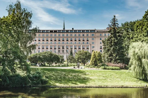 Large building with 4 stories of windows with an outdoor grass area and a small pond