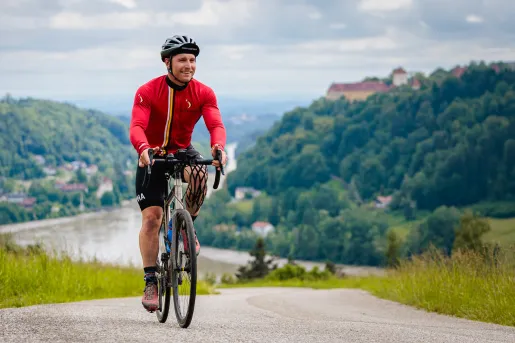Man riding a bike on an asphalt road, with mountains of trees behind him