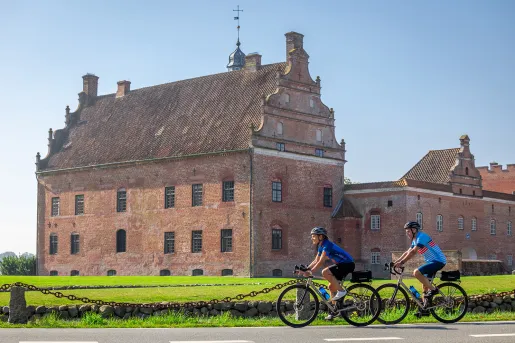 Two bikers in front of a large red building in the middle of a grass field