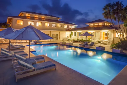 Outdoor pool with blue reclining chars with an illuminated building in the back