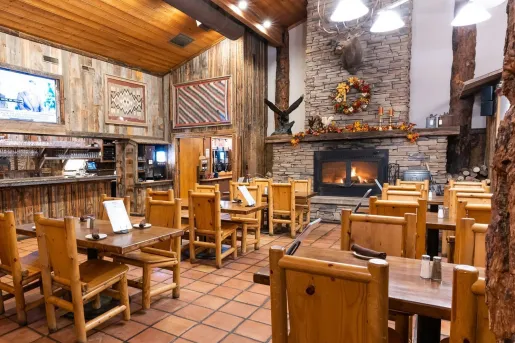 Indoor dining area in a lodge-style hall, with a stone fireplace in the background