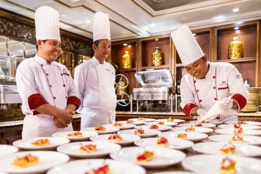 Three chefs smiling while decorating a table full of plates