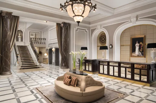 Hotel lobby with a staircase on the left and a brown, cushioned chair in the center